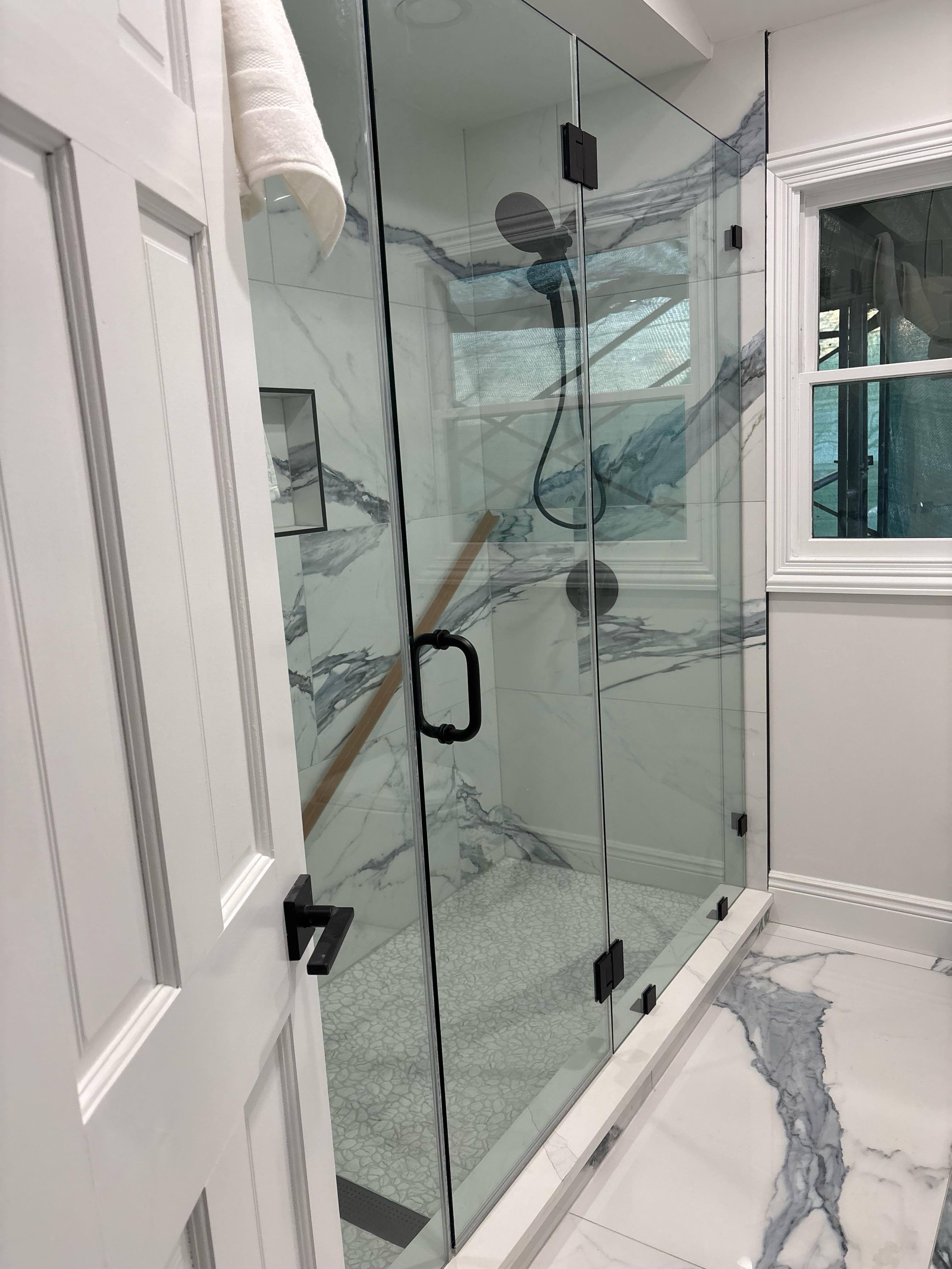 Frameless glass shower door with marble tile and matte black hardware in Brooklyn bathroom